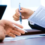 Person reviews car loan papers and a calculator at a kitchen table for an upside-down trade-in calculator.
